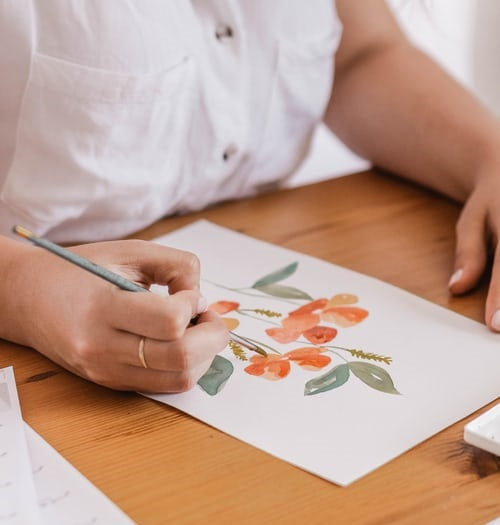 Woman holding paint brush, painting with watercolors on paper.