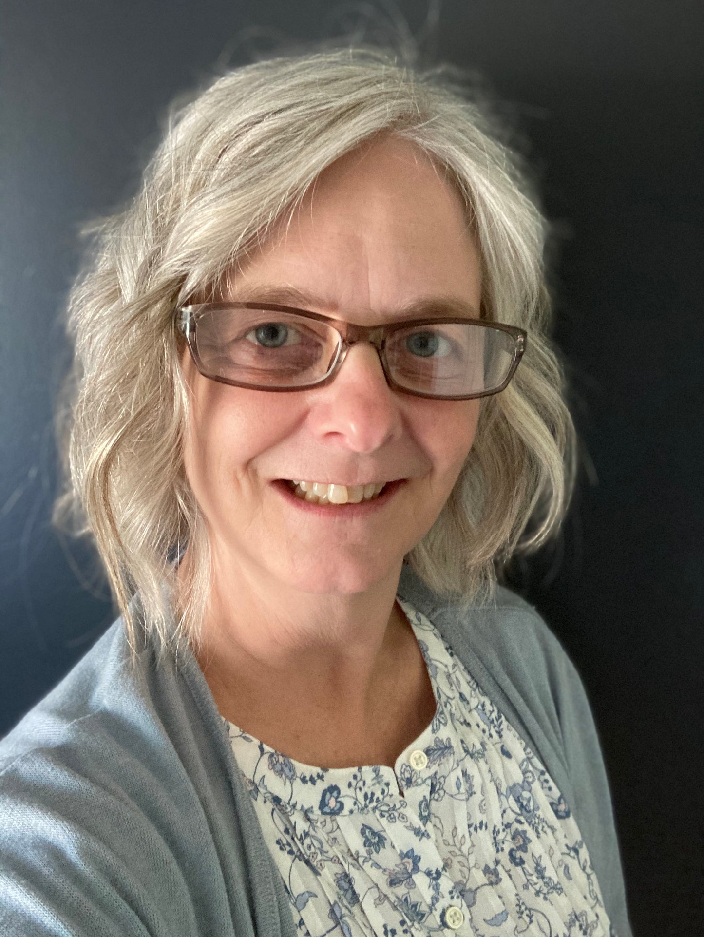 Artist Tonya Henderson wearing a light blue cardigan over a floral shirt against a dark background, your host for this event.