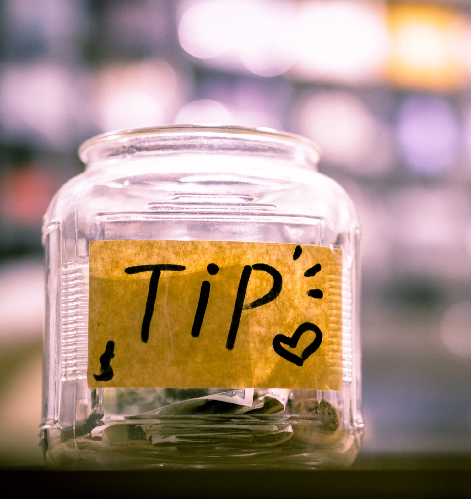 A photo of a jar with a sign that says "tip" with dollars inside.