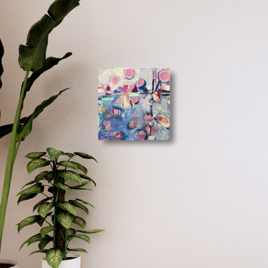 Original abstract painting in blue and pink by artist Tonya Henderson hanging on a wall with a plant in the foreground.