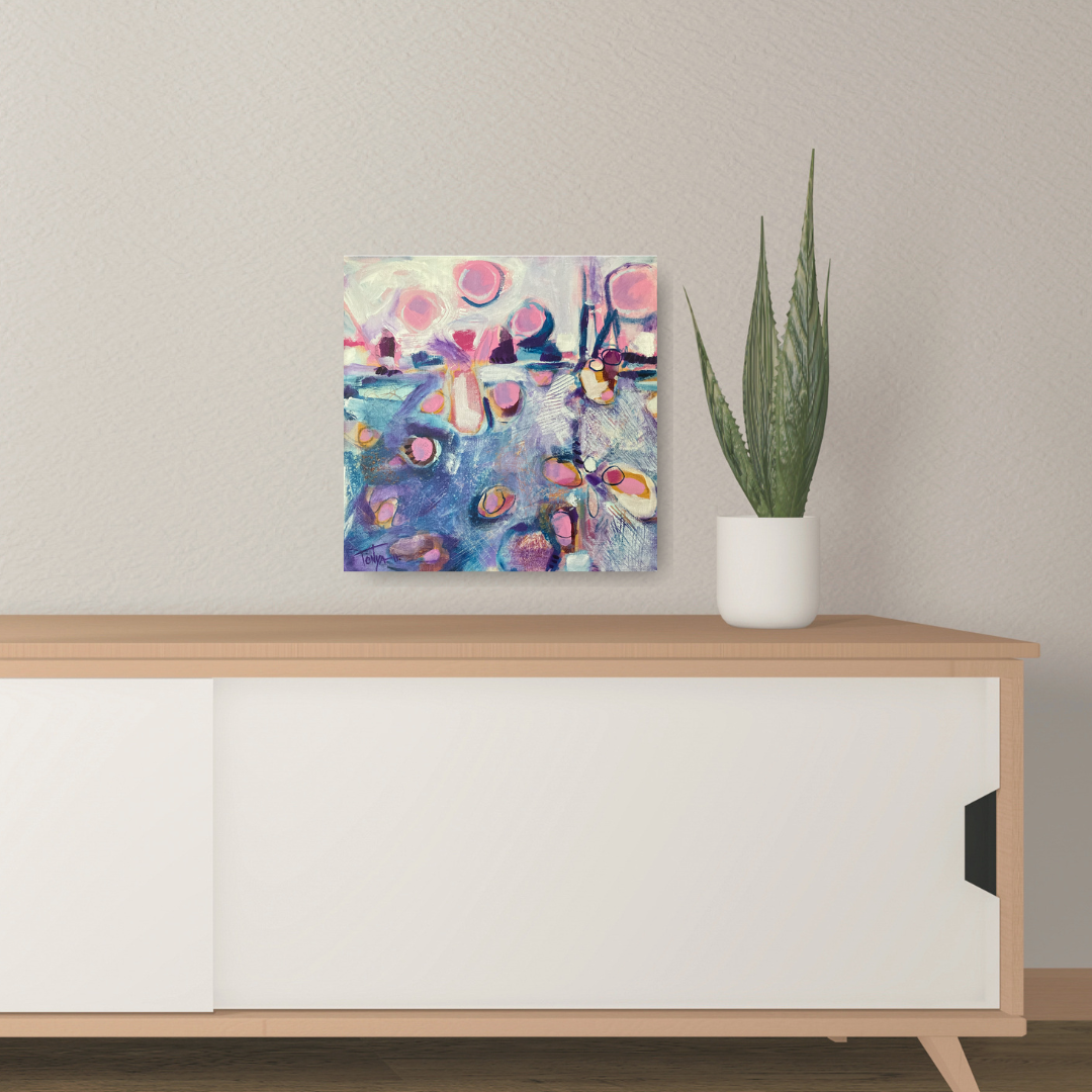 Blue and pink abstract acrylic painting by artist Tonya Henderson hanging on a wall above a wooden cabinet with a plant.