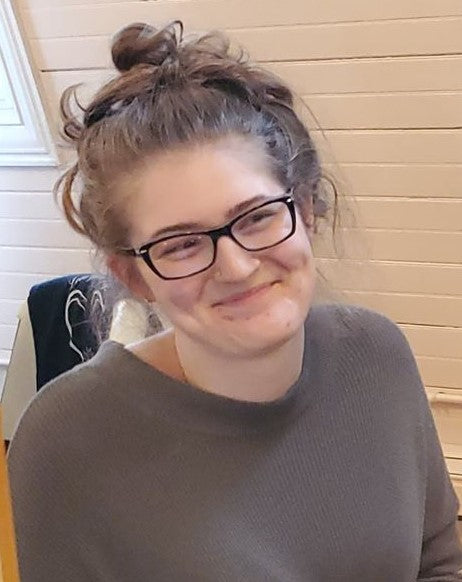 A woman sitting in a chair with her hair up wearing glasses and a sweater.