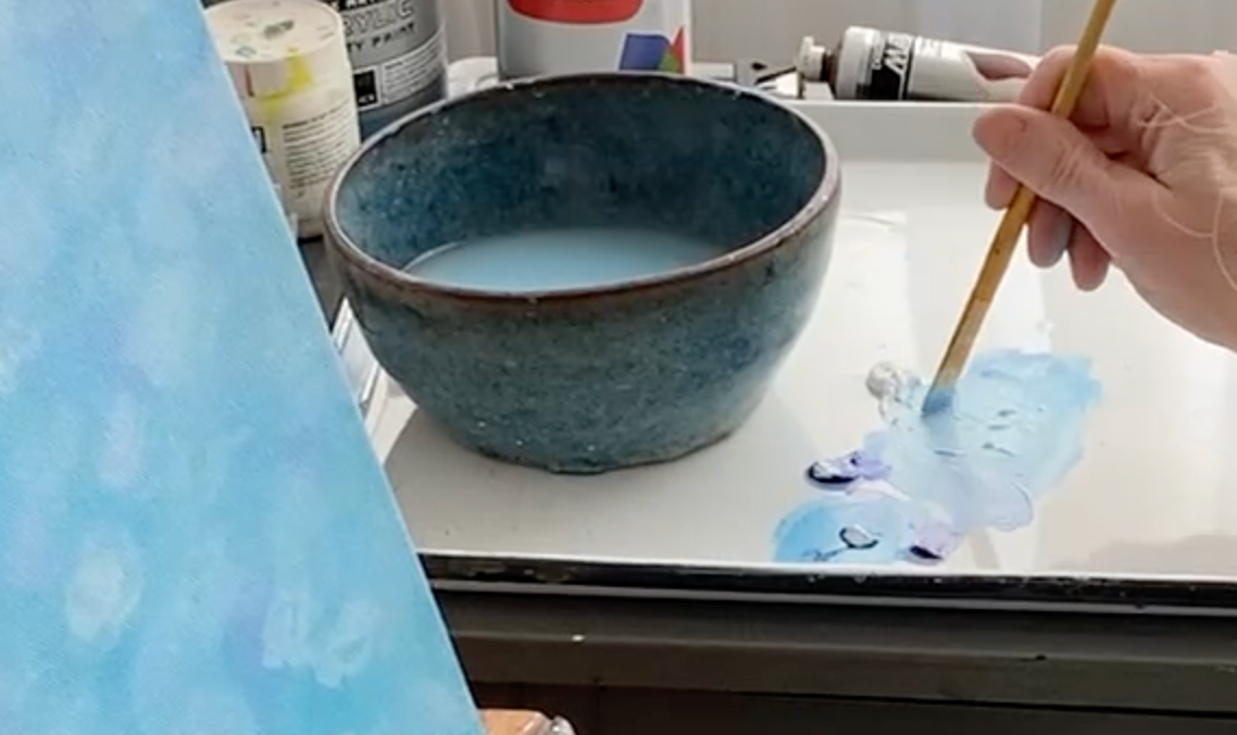 Artist Tonya Henderson mixing paint with a brush on a palette with a blue water bowl nearby and the edge of the painting she is working on.