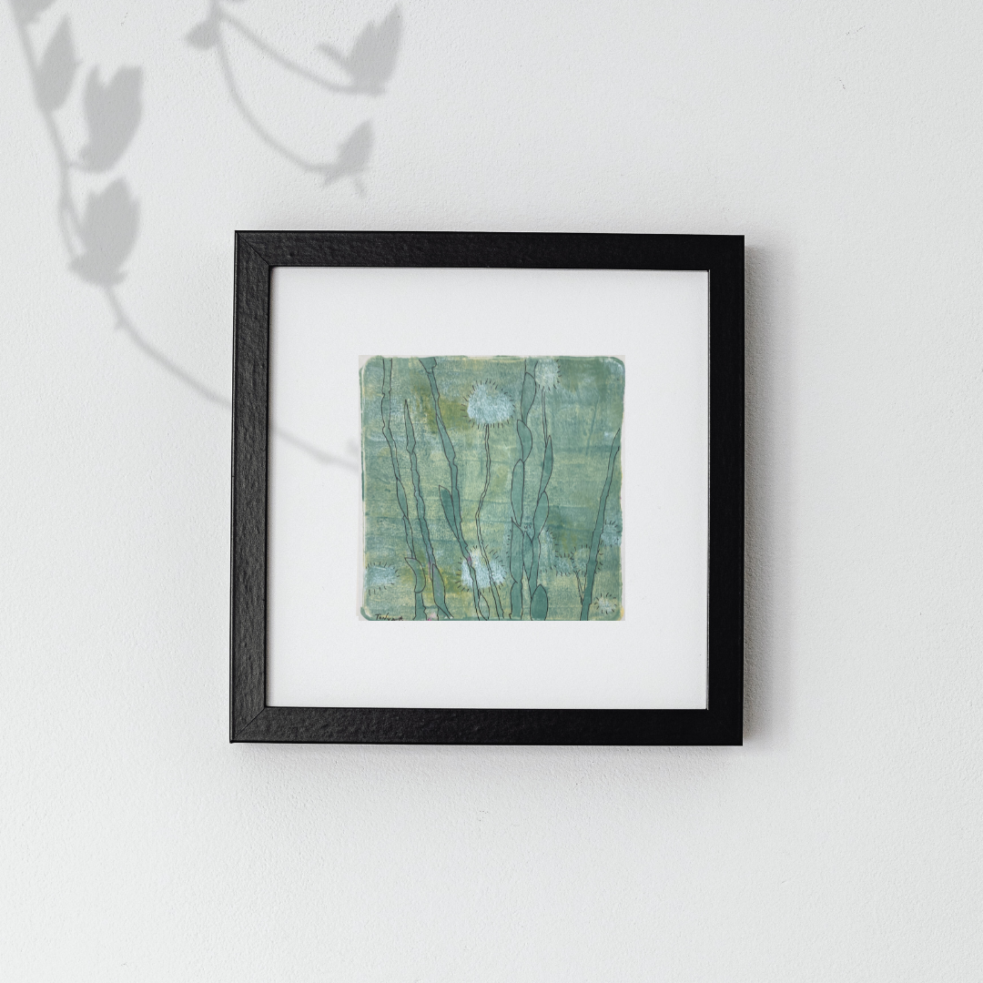 Framed artwork with a green abstract mixed media landscape artwork on a white wall.