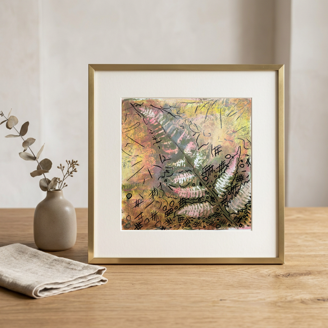 Framed abstract art piece on a wooden surface with a vase and cloth in the background