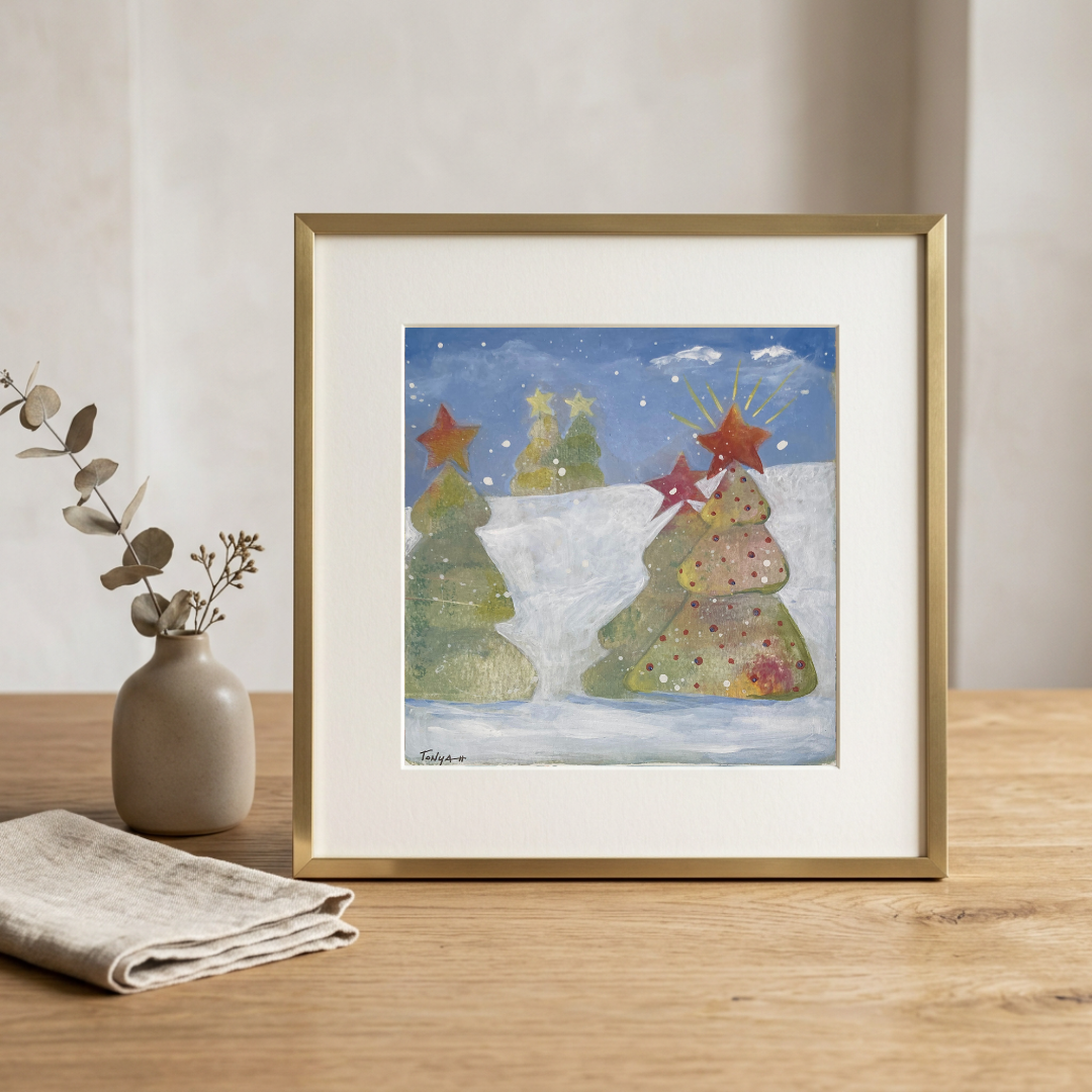 Framed artwork of Christmas trees on a wooden table with a vase and cloth.