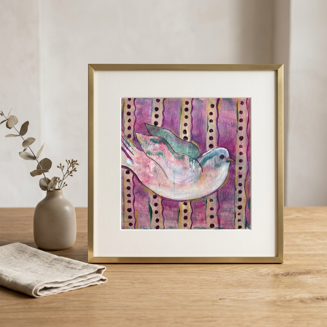 Framed artwork of a colorful bird on a striped background on a wooden table.