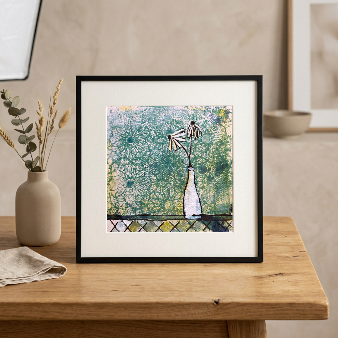 Framed abstract artwork on a wooden table with a vase and cloth in the background