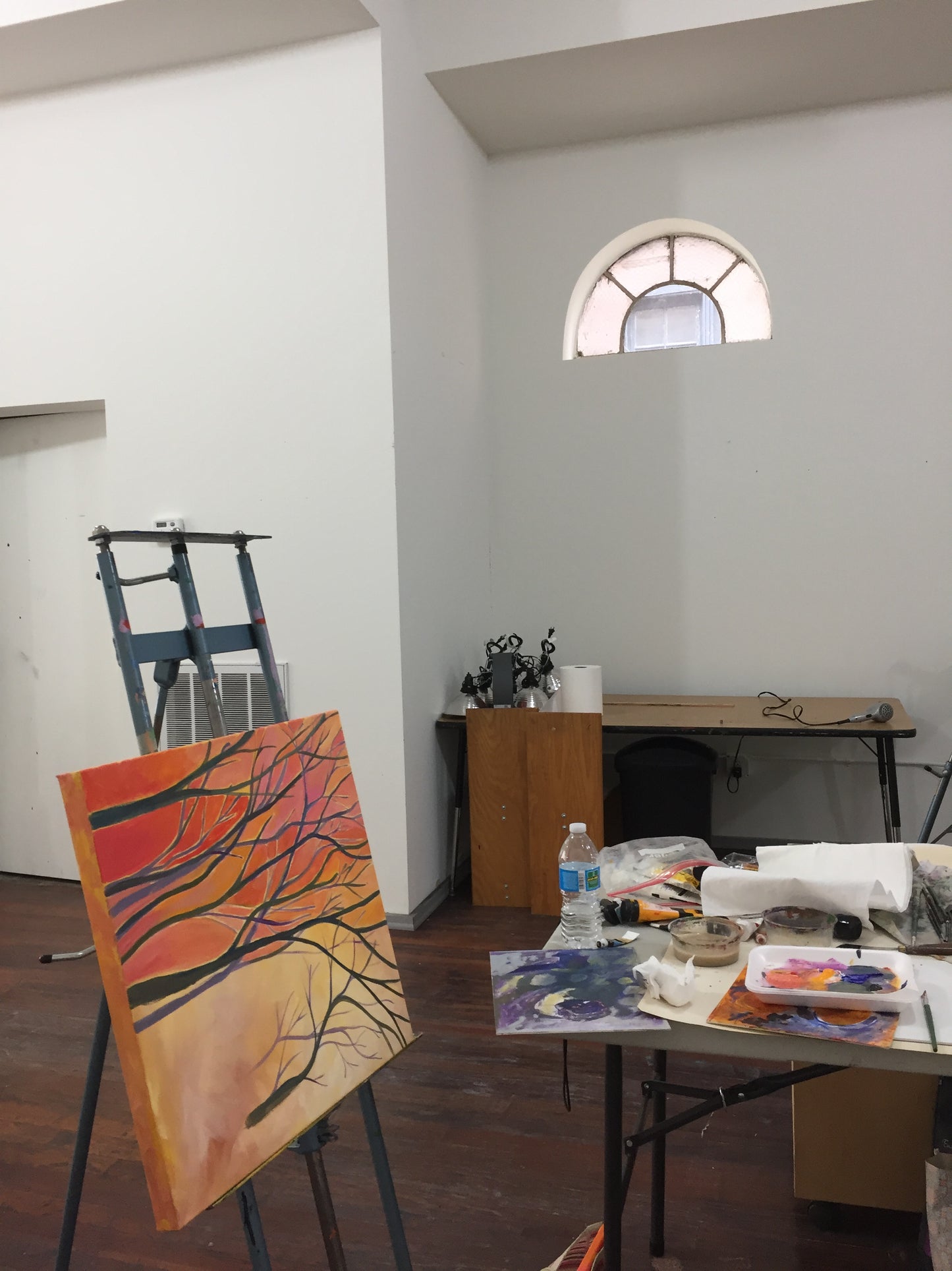 Art studio with a painting of trees on an easel and various art supplies on a shelf as art class gets underway with instructor Tonya Henderson.