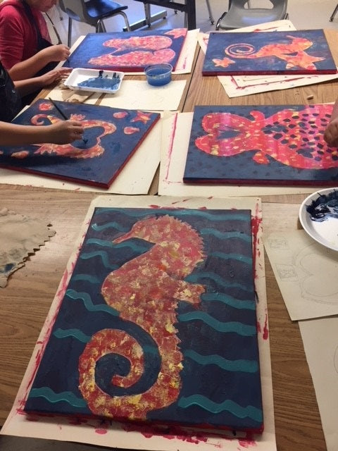 Table covered in artworks with sea creatures painted in orange, red, with a dark blue background.