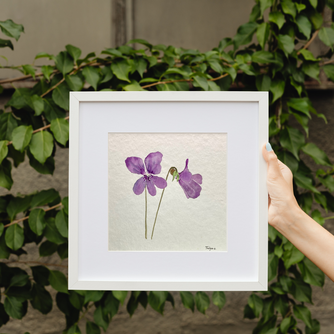 Original watercolor painting of purple flowers by artist Tonya Henderson being held by a hand with green foliage in the background.