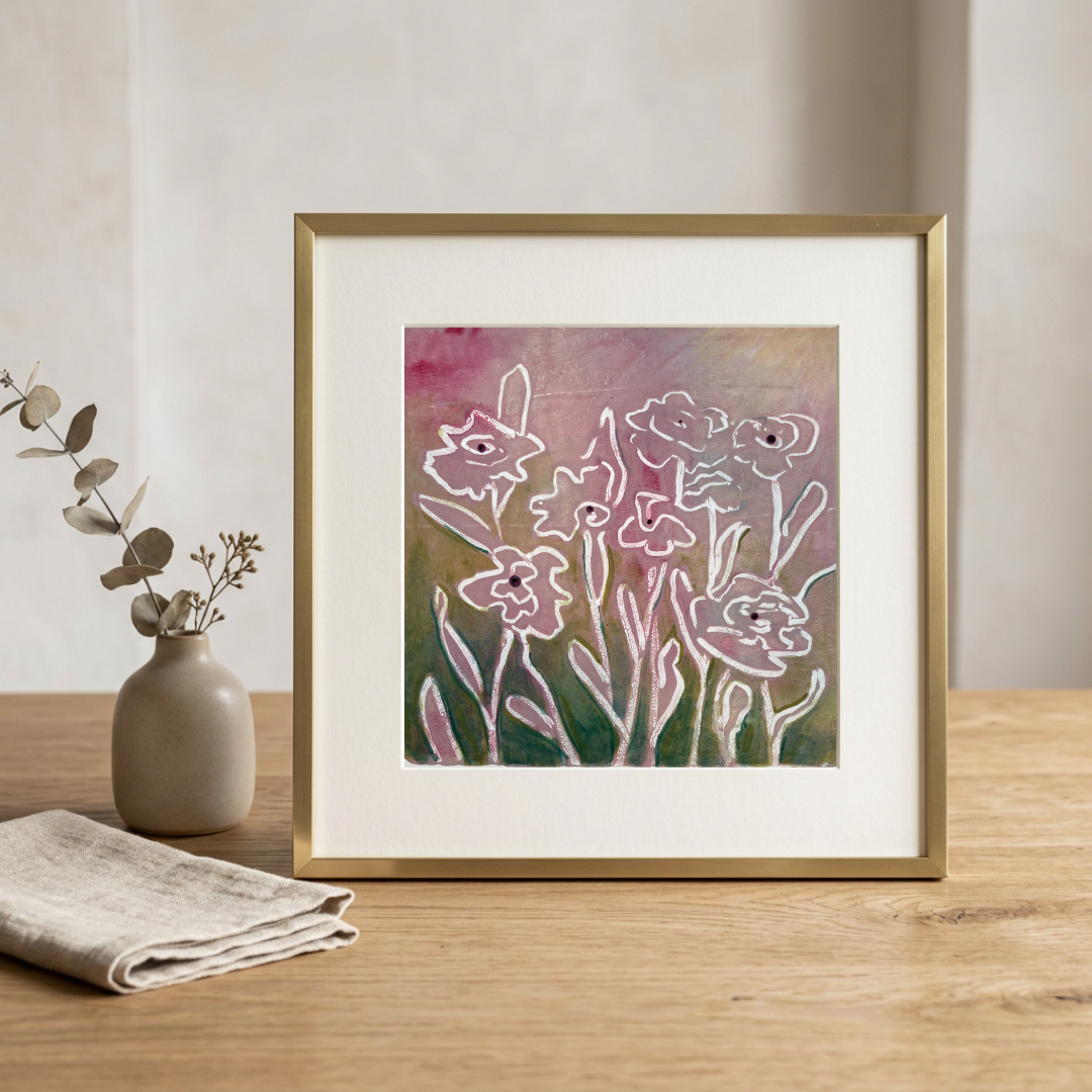 Framed floral artwork on a wooden table with a vase and cloth in the background