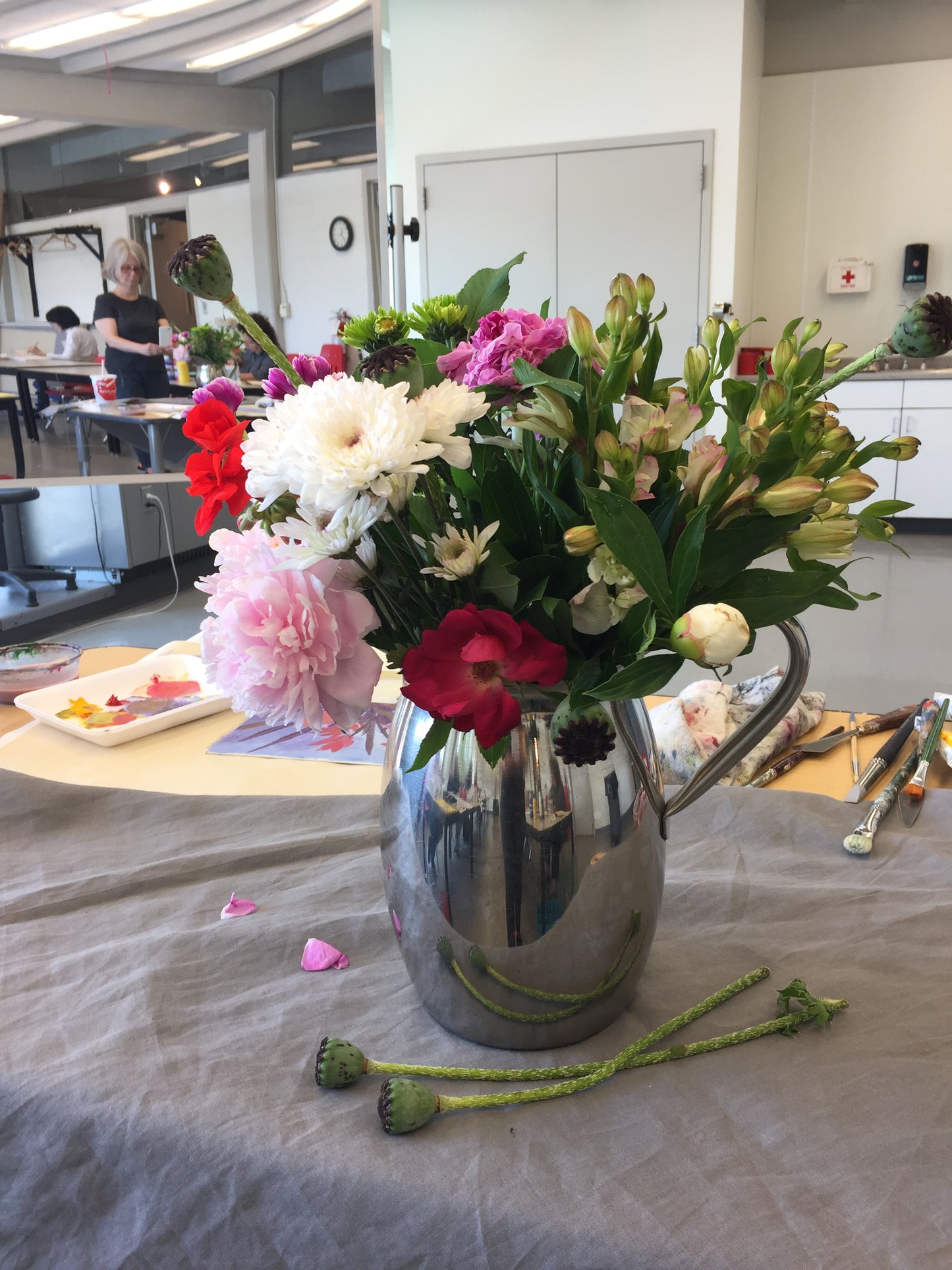 Bouquet of flowers in a silver vase on a table with a blurred indoor background and art instructor Tonya Henderson squeezing out paint colors.