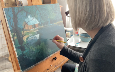 Artist Tonya Henderson brushing paint on a landscape scene called "Cabin in the Woods" which is sitting on an easel.