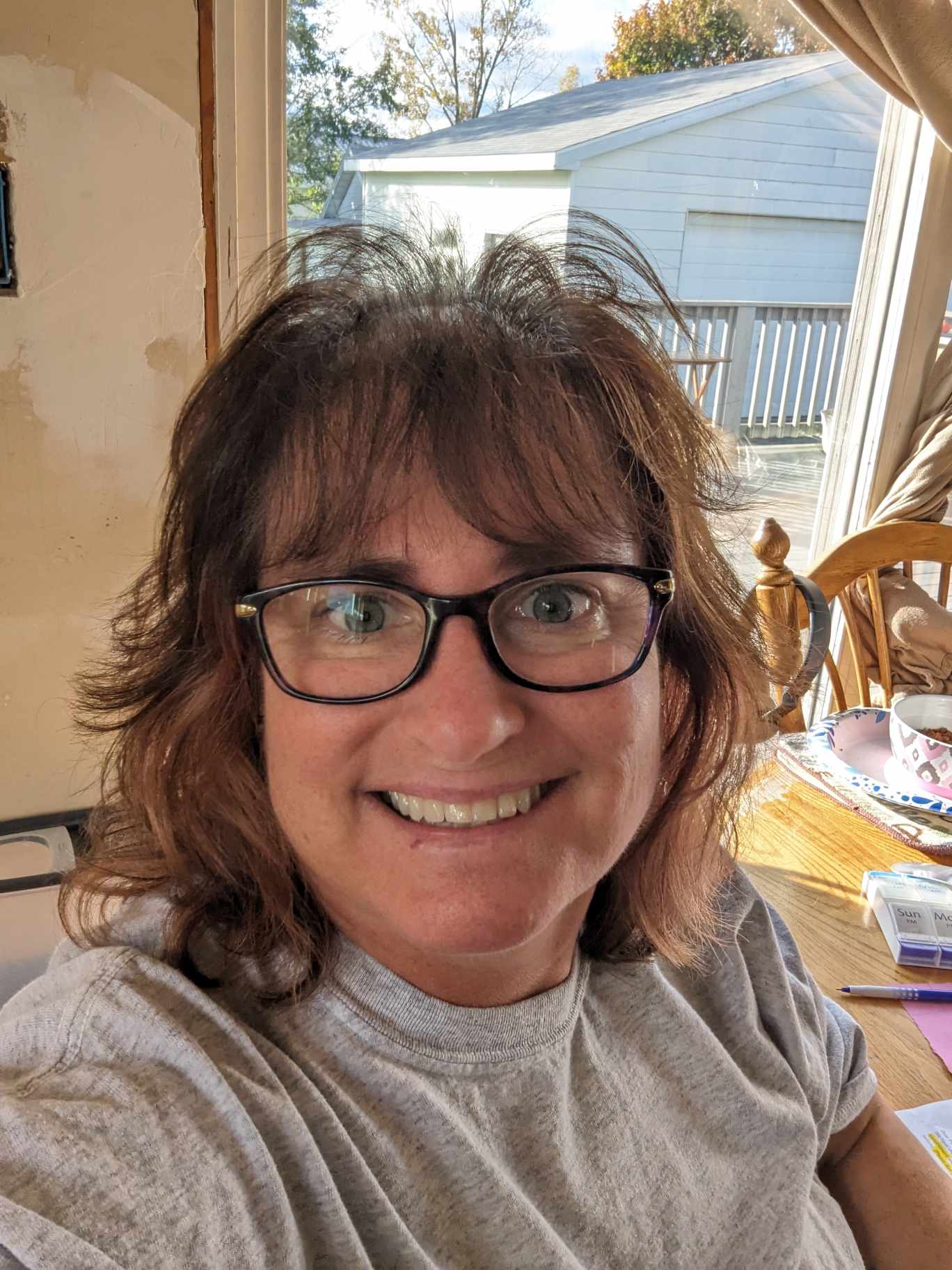 Woman sitting at dining table with glasses wearing a tshirt.